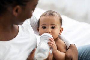 Woman in white shirt holding a baby who's drinking out of a white bottle